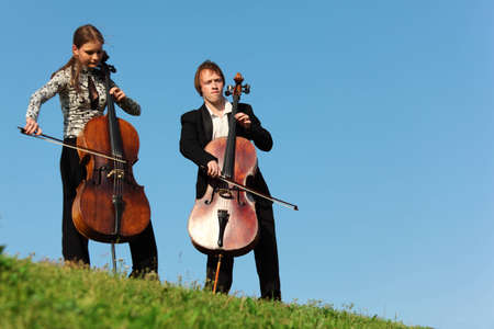 Two violoncellists play on grass against  skyの写真素材