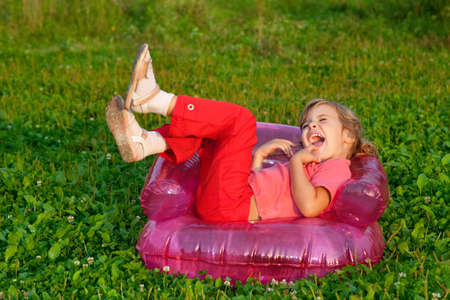 young girl playing tricks in inflatable armchair outdoorsの写真素材