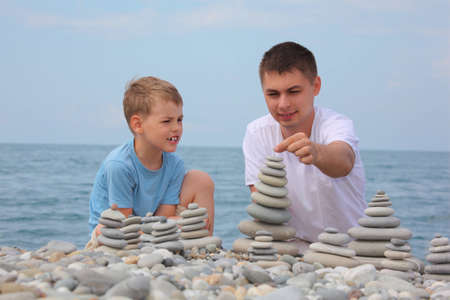 father and son builds  stone stacks on pebble beachの写真素材