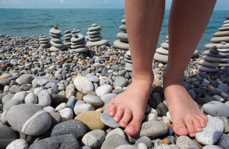 two childish legs and stone stacks on pebble beachの写真素材