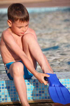 boy puts on flippers on border of poolの写真素材