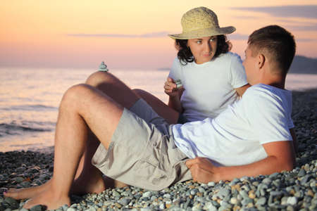 young man and woman in straw hat design pyramids from pebble on stony beach in evening