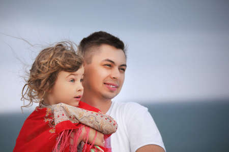 young man protects little girl from wind on seacoastの写真素材