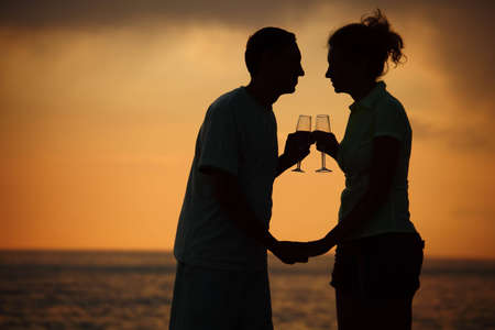 Silhouettes of man and woman with glasses on sea sunsetの写真素材