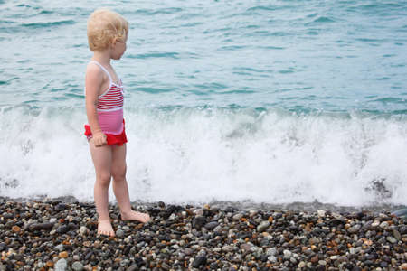 child stands on pebble beachの写真素材