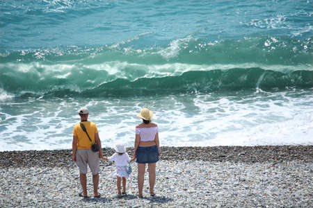 Parents with child stand on seacoast and big wave,  rear viewの写真素材