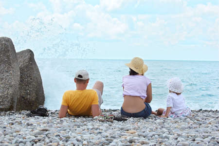 Parents with child sit on seacoast,  rear viewの写真素材