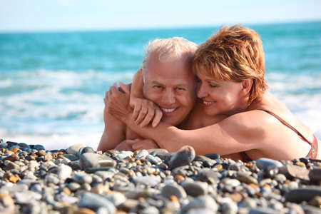happy aged pair lie on pebble beach, focus on womanの写真素材