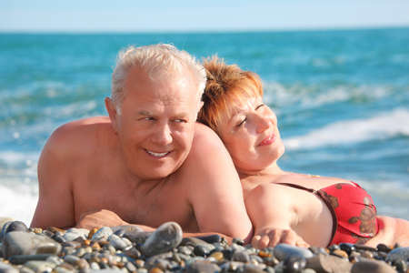 happy aged pair lie on pebble beachの写真素材