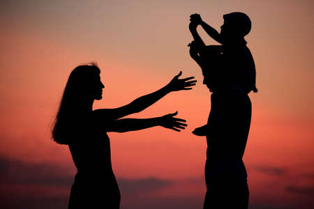 Silhouettes of parents with child against  sea declineの写真素材