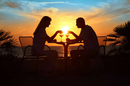 Female and man's silhouettes on sunset sit at table with two glasses outdoorの写真素材