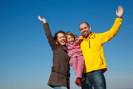 Happy parents together with a daughter with the hands lifted upwards a bright sunny day against the blue sky.の写真素材