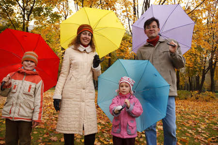 Family from four persons in autumn park with multi-coloured umbrellas.の写真素材