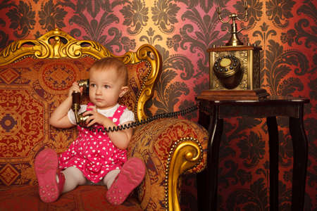 Little girl in red dress talking vintage phone. Interior in retro style. Horizontal format.の写真素材