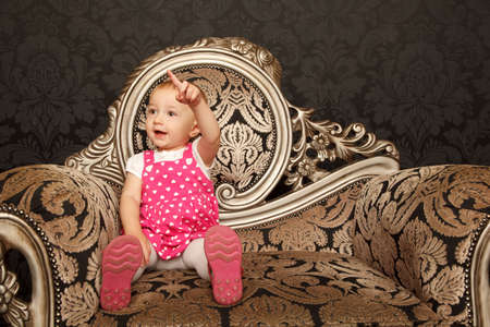 Little girl in red dress sitting on retro armchair with finger pointing up.の写真素材