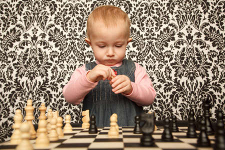 Portrait of little girl in denim dress playing chess. Horizontal format. Indoor.の写真素材