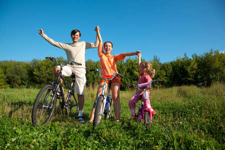 Parents with the daughter on bicycles in park a sunny day. Have joyfully thrown up hands.の写真素材