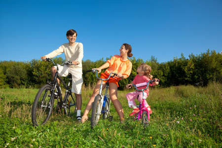 Family from three persons on bicycles in the country. Mum with a daughter look at the daddy.の写真素材