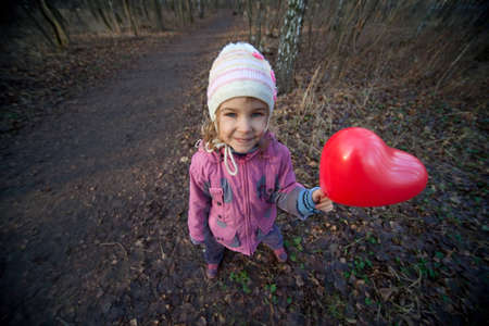 Small girl with inflatable red heart in terrible dark forestの写真素材