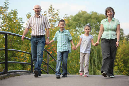 family with two children is walking on bridge in early fall park. family is handies.の写真素材