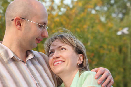 man and woman in early fall park. man is embracing smiling woman and looking at her