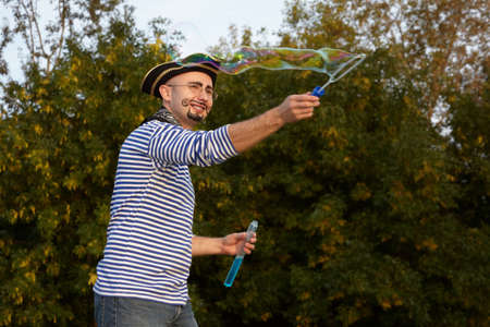 joyful man with drawed beard and whiskers in pirate suit is blowing soap bubbles.の写真素材