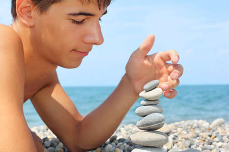 teenager boy lying on stony seacoast, creates pyramid from pebbleの写真素材