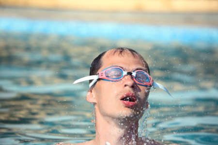 young man in watersport goggles swimming in pool, ñome up from water, taking breathの写真素材
