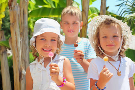 Smiling children three together eat lollipop in parkの写真素材