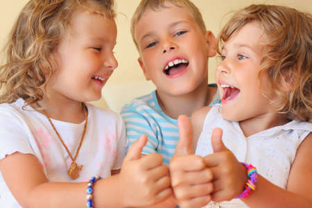 Smiling children three together in cosy room shows îê gesture