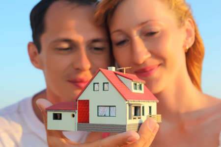 Young woman and man keeping in hands model of house with garageの写真素材