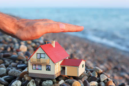 model of house with garage on stony beach in evening, Man's hand over houseの写真素材