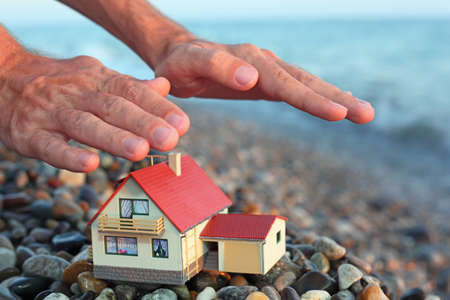 model of house with garage on stony beach in evening, Man's hands over houseの写真素材