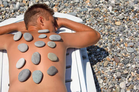 young man sunbathes on beach with stones on backの写真素材