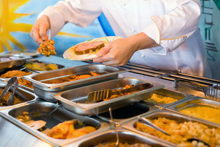 Hands of cook putting in plate vegetable ragout in public catering restaurant