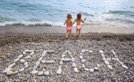Inscription from stones BEACH at stony coast, two pretty little girls on seacoastの写真素材