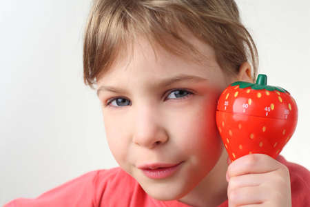 little  girl in red shirt holding in hand plastic kitchen timer strawberry and looking at cameraの写真素材