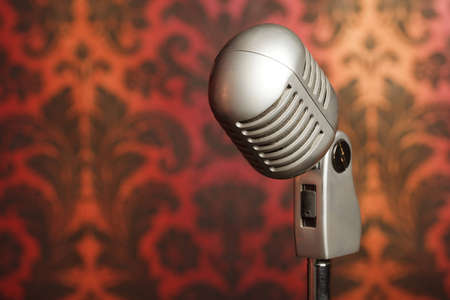vintage metal microphone on a stand photographed against a background of yellow-red ornament wallpaperの写真素材