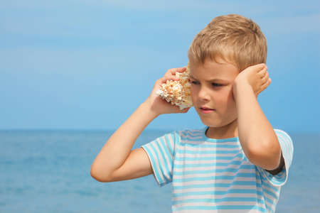 little boy with shell listening noise of sea. sea in out of focus.の写真素材