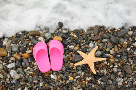 pinky slippers and starfish on pebbles near water. foam in top of image.の写真素材