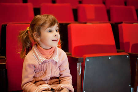 Smiling little girl sitting on armchairs at cinemaの写真素材