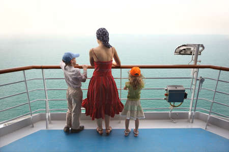 little boy and girl with mother standing on ship deck and looking at horizonの写真素材