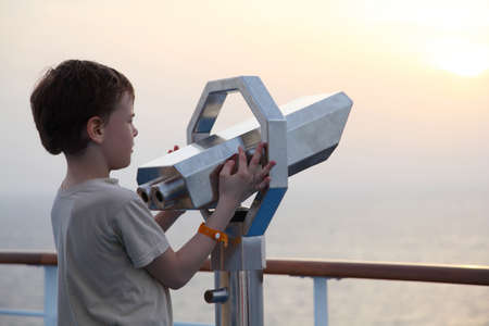 little boy standing near binocular and looking into the distance side view half bodyの写真素材