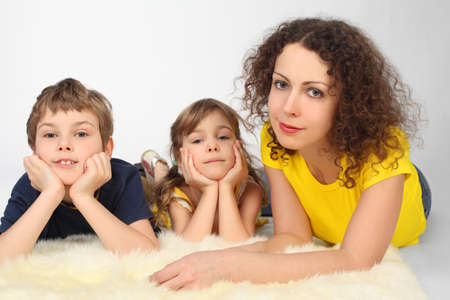 young mother daughter and son lying on white fell and looking at cameraの写真素材