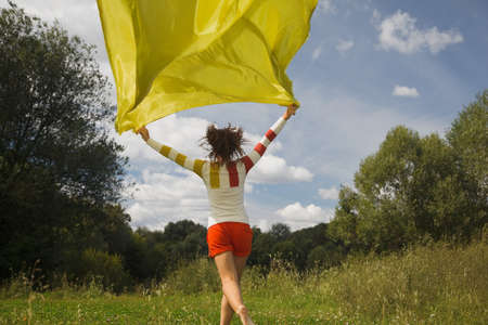 young woman in sunny summer day runnig with yellow fabric in hand, whiffle fabricの写真素材