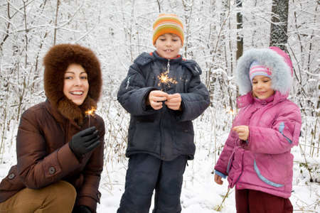 young woman with boy and little girl with Bengal fires in hands in winter in woodの写真素材
