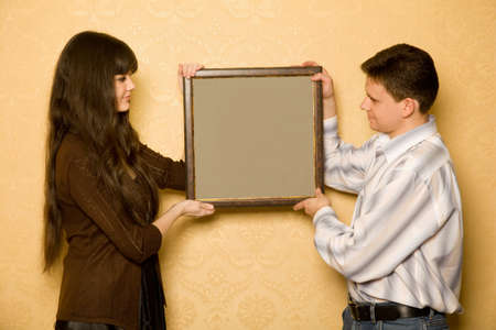 young beautiful woman and smiling man with picture in frame in hands, looking at picture with sideの写真素材