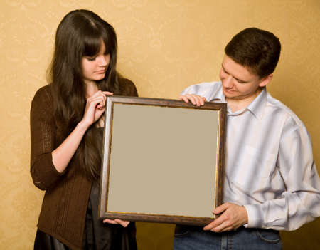 young beautiful woman and smiling man with picture in frame in hands, looking at pictureの写真素材