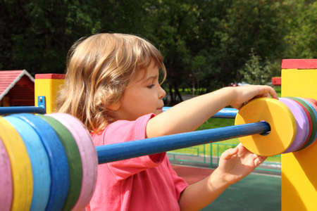 young girl playing at playground in summer sunny day, moves colour rings for mathematic counting