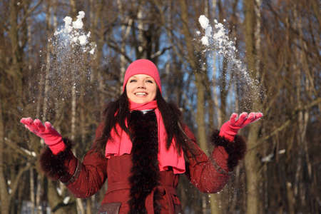 young beauty girl in pink scarf and hat smiling throwing up snow, outdoor at winter day